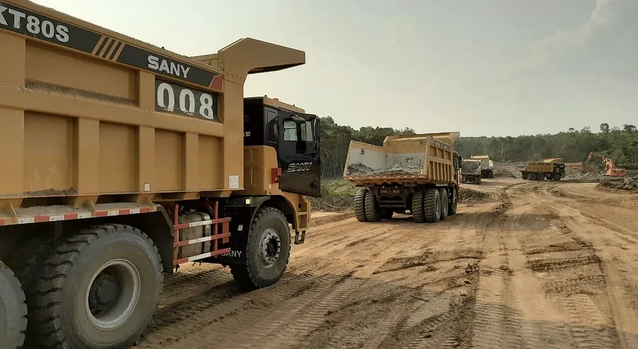Loaded haul trucks in convoy on a graded laterite haul road cut through forest.