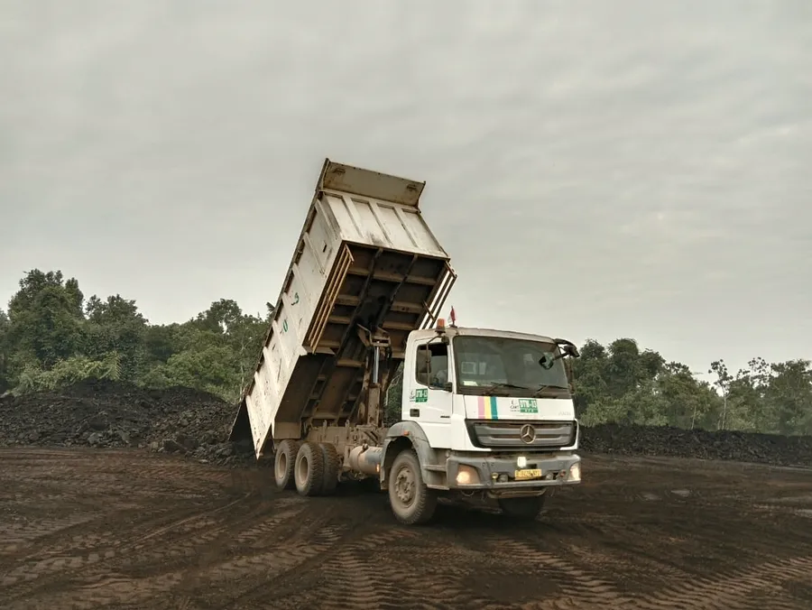 Tipper truck with its body raised, discharging its load onto a coal stockpile.